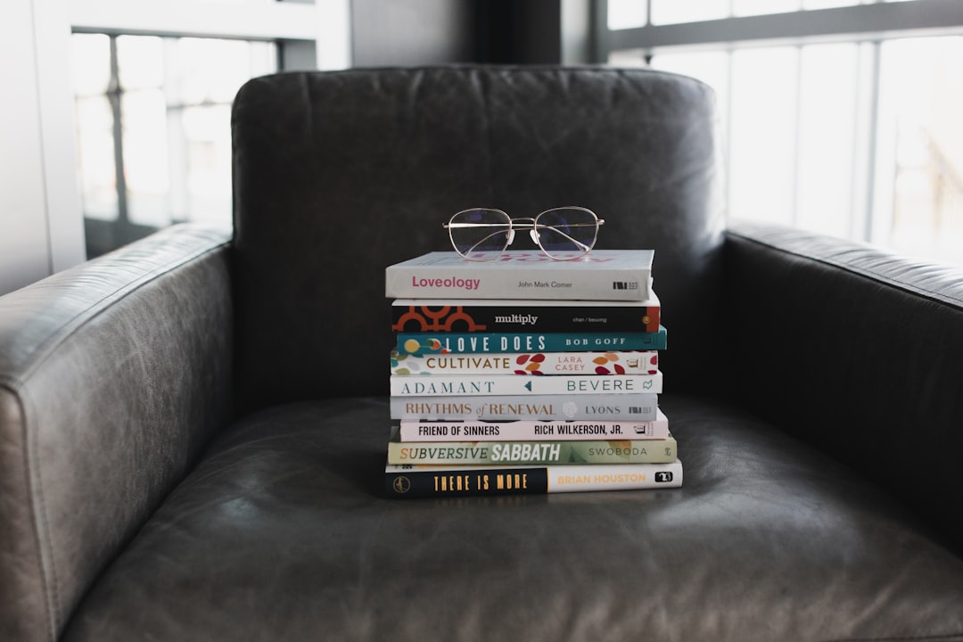stack of books on a comfy-looking gray leather chair with glasses on top of the stack 