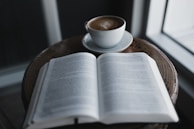 Wooden reading table at Reigning Pages Book Shoppe with an open book and a steaming cup of coffee.