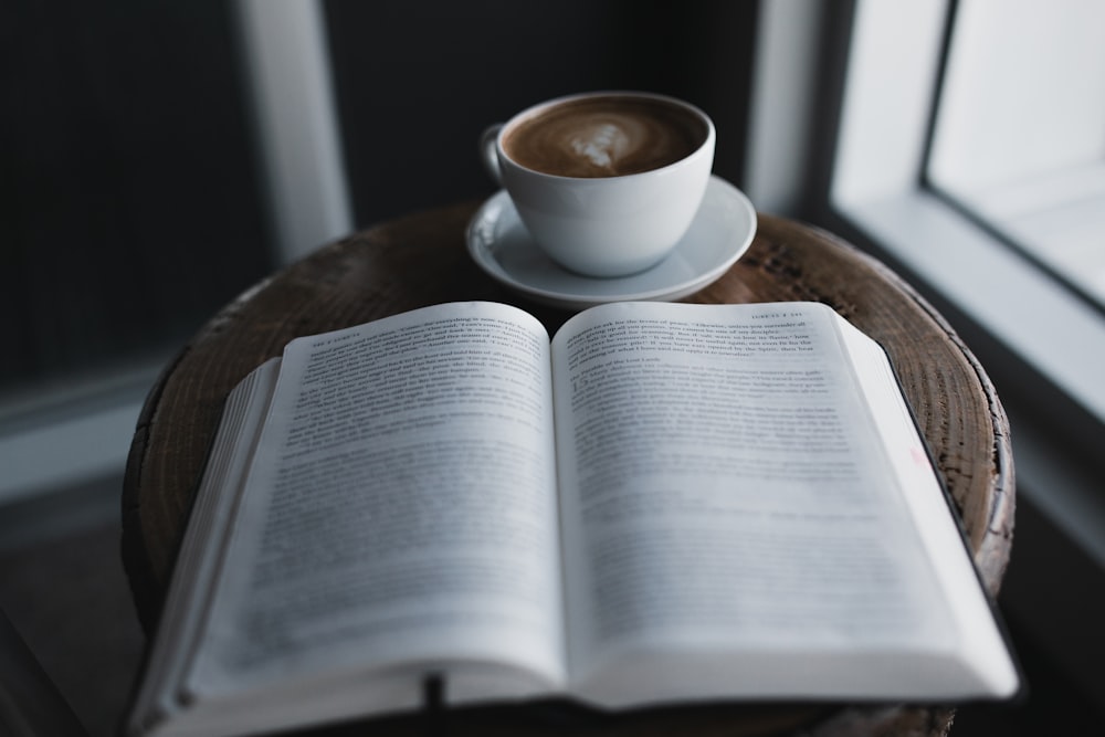 white ceramic cup on white ceramic saucer beside book