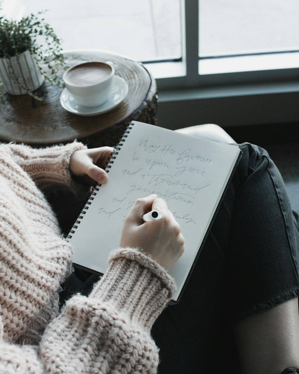 person in white knit sweater writing on white paper