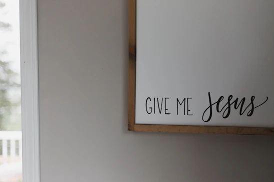 A cozy living room wall adorned with a framed Christian scripture print glowing softly in natural light.