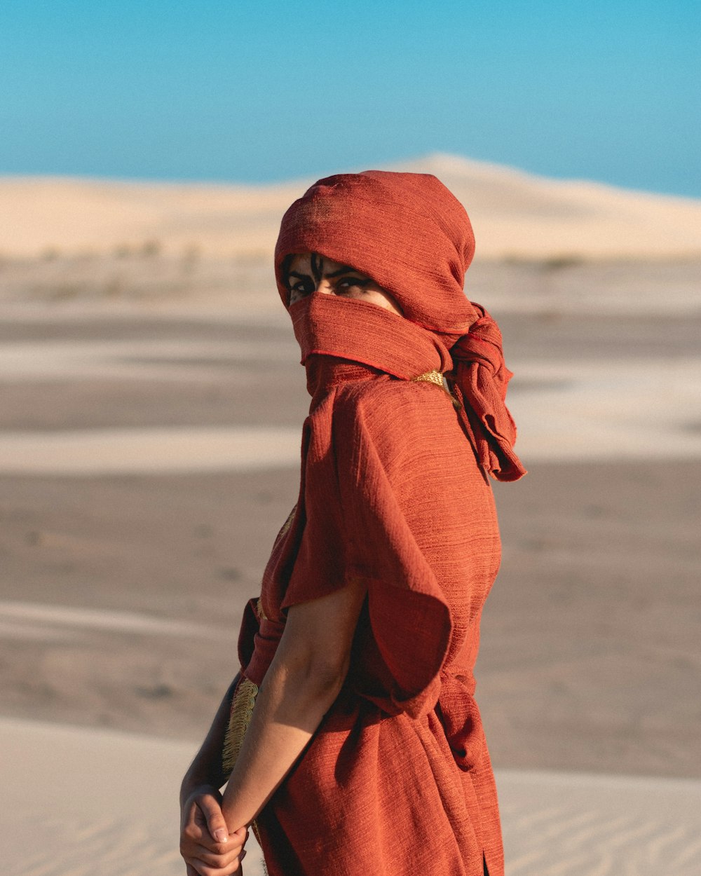woman in orange hijab standing on brown sand during daytime