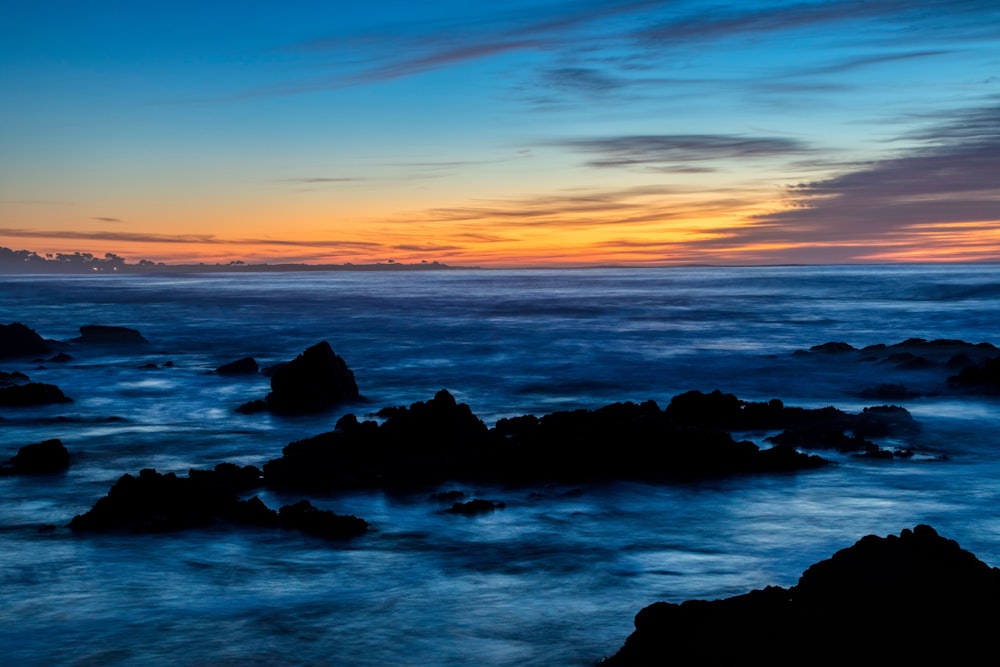 silhouette of rocks on sea during sunset