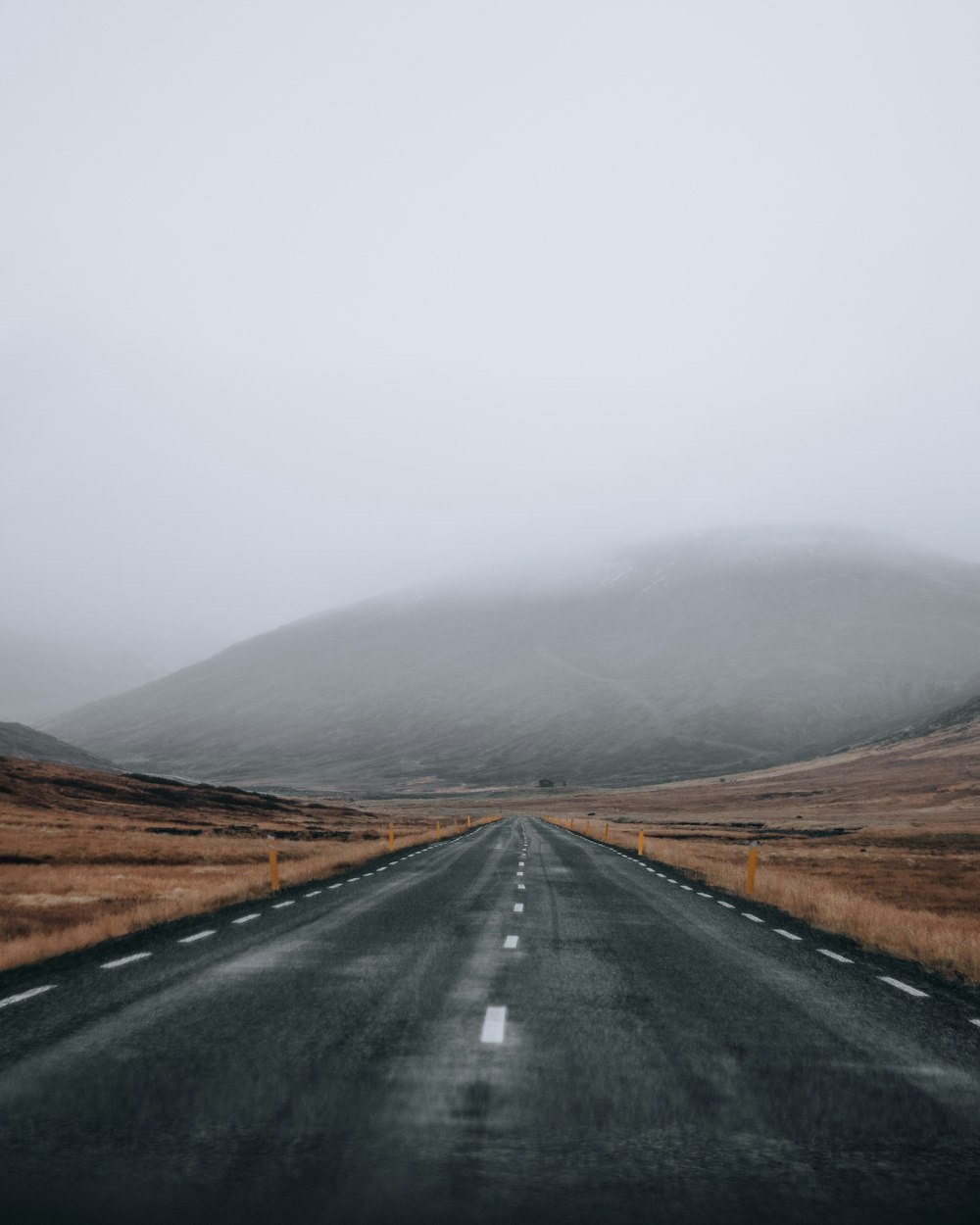 black asphalt road between brown grass field during daytime