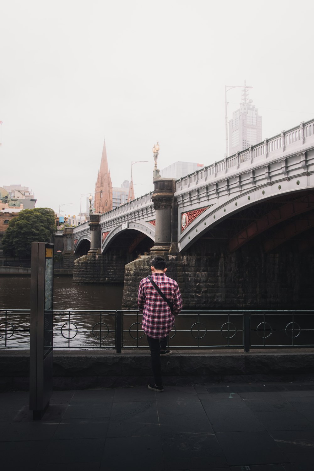 woman in pink and white checkered dress shirt standing on bridge over river during daytime