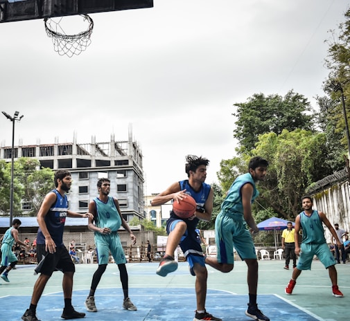 Players competing fiercely in a sunny outdoor basketball game surrounded by cheering families.