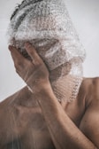 A person with their face covered in bubble wrap, one hand touching the side of their face, creating a surreal and thought-provoking visual composition.