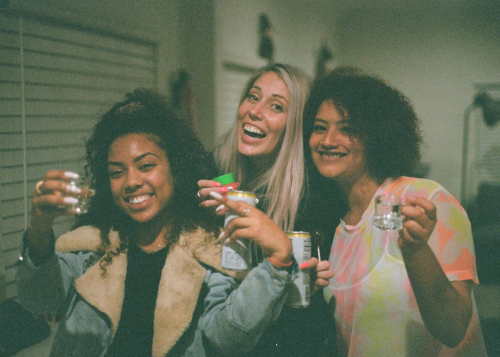 3 women holding clear glass bottle