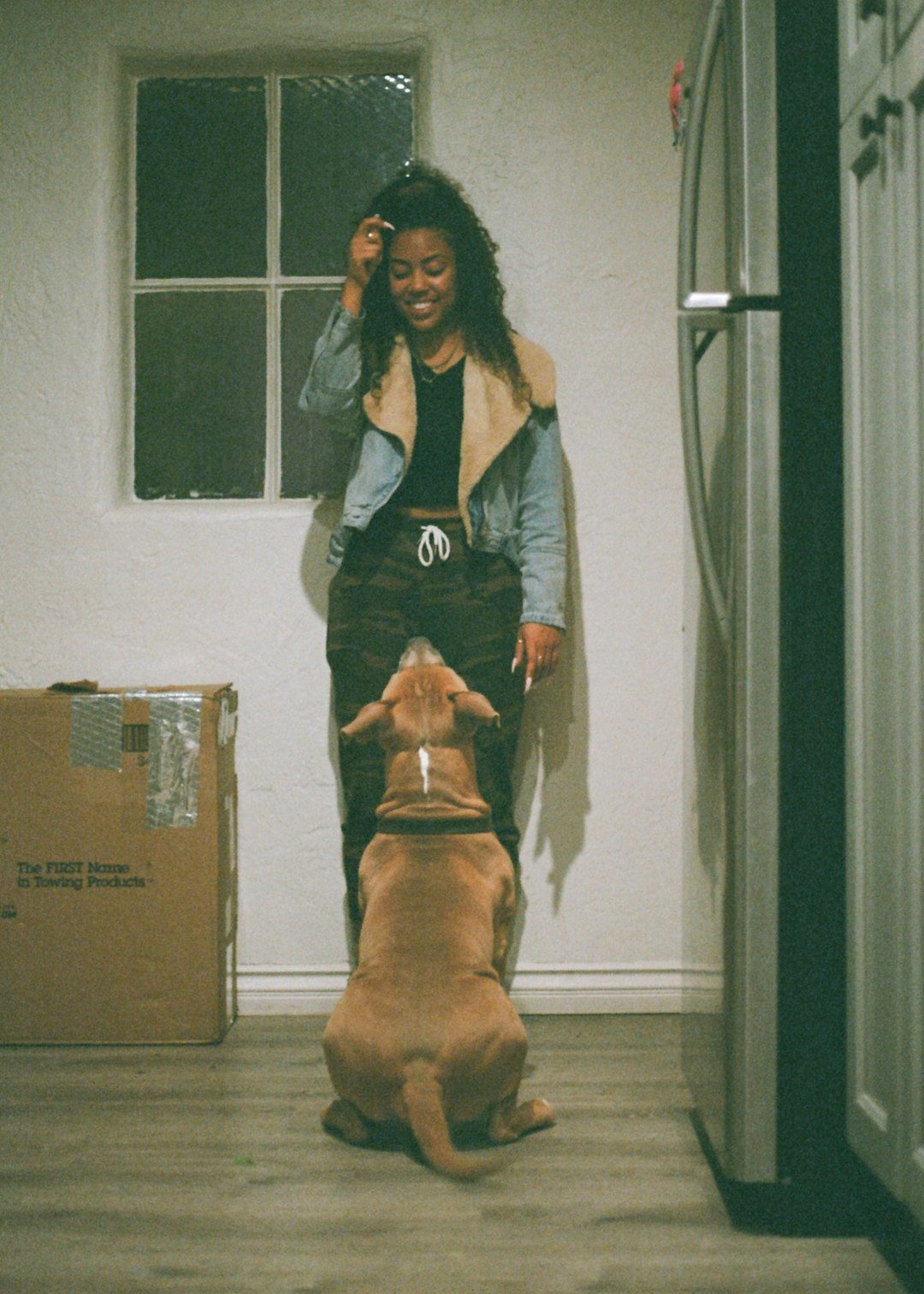 woman in gray jacket standing beside brown short coated dog