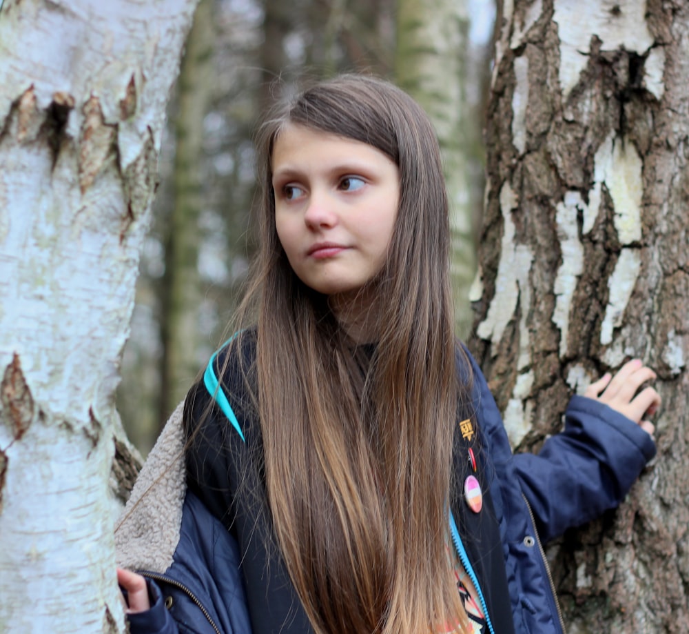 woman in black jacket leaning on brown tree