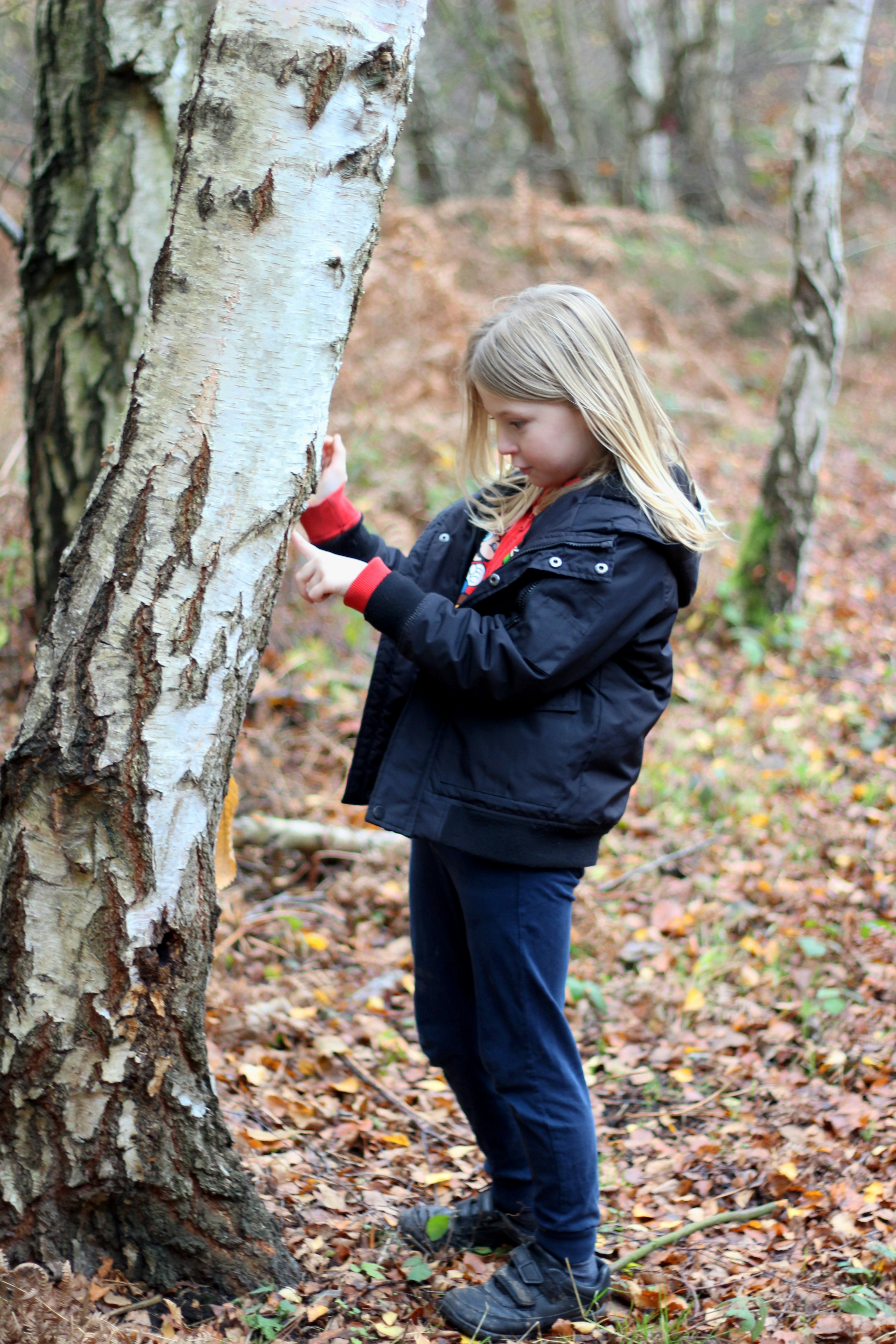 Frau in schwarzer Jacke und schwarzer Hose neben Baum
