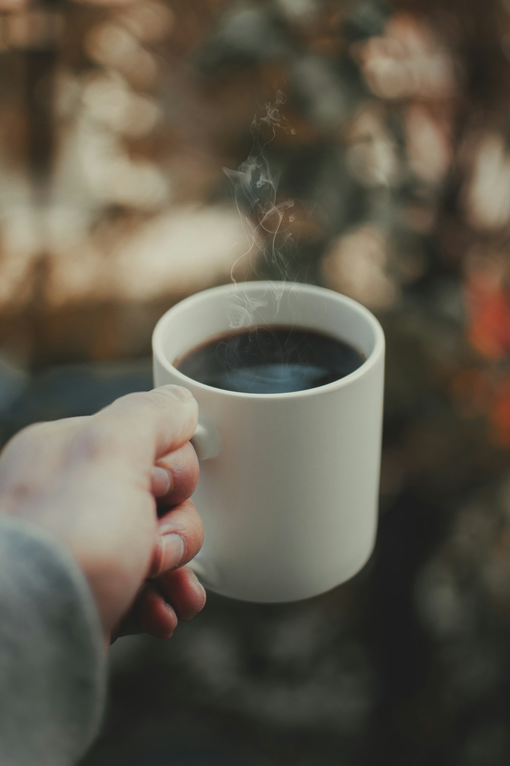 person holding white ceramic mug with brown liquid