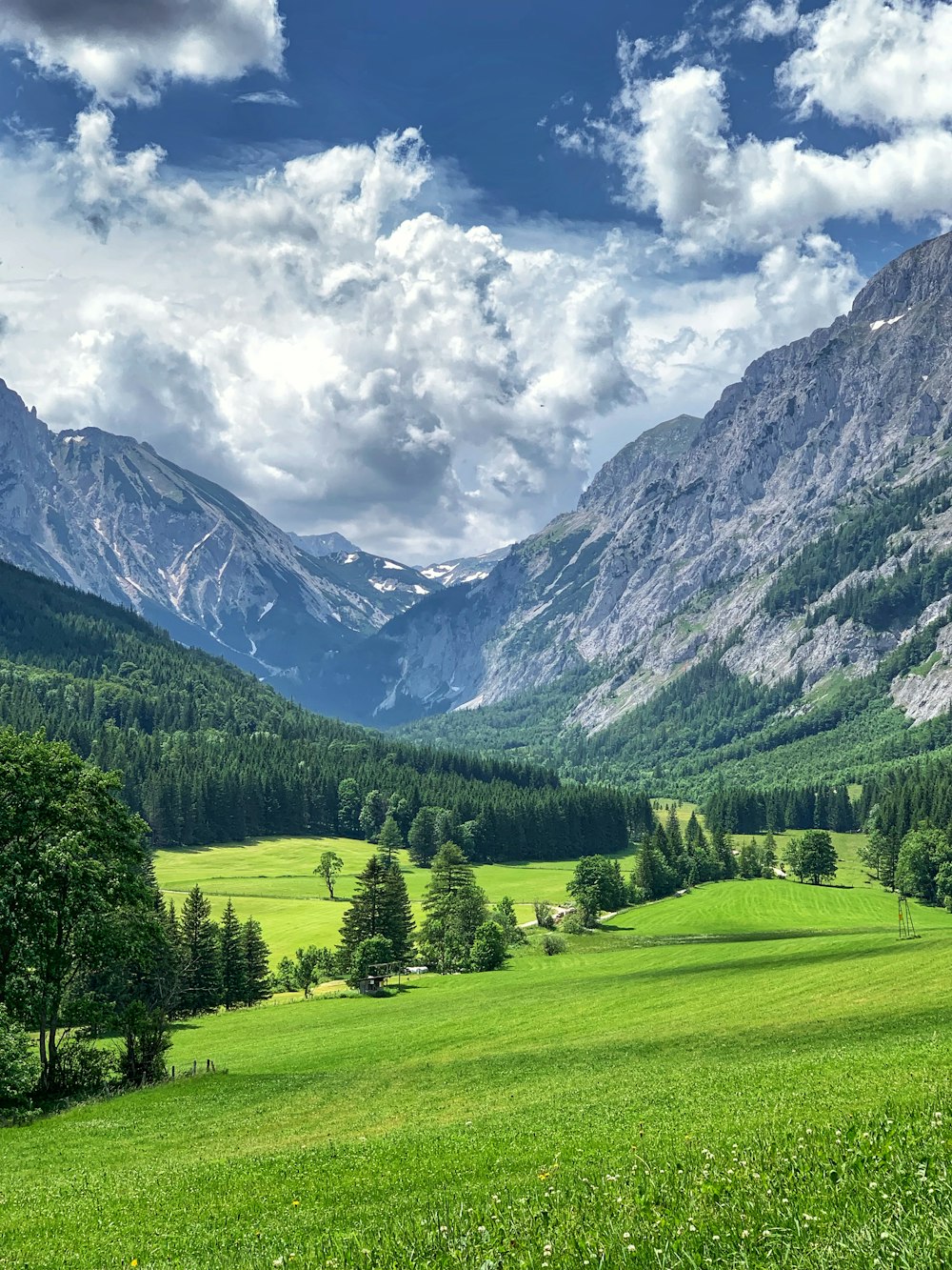 green grass field near mountain under white clouds during daytime