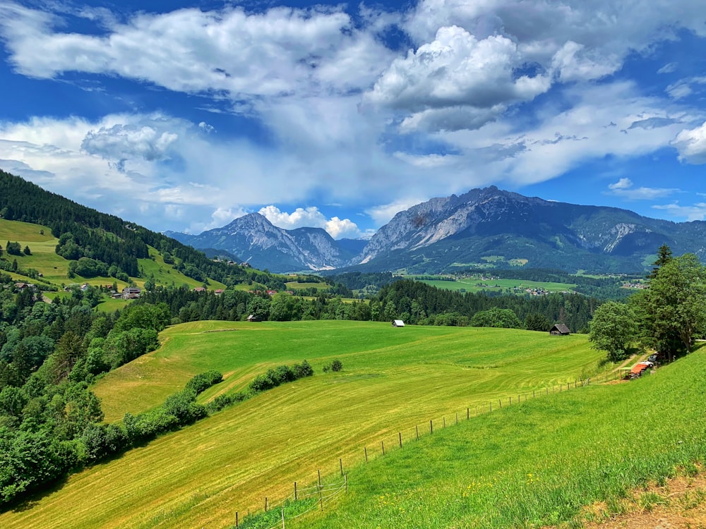 green grass field near mountain under blue sky during daytime