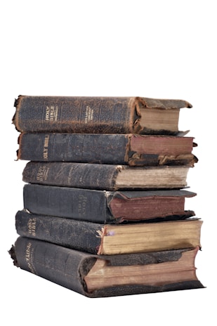 A stack of old, worn books with dark covers and frayed edges. The binding and pages show significant aging and use.