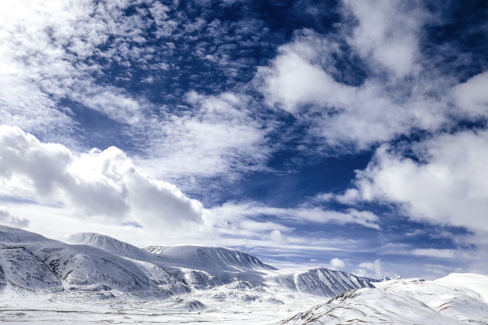 montagne enneigée sous les nuages blancs et le ciel bleu pendant la journée