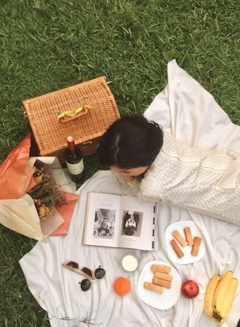 A scenic outdoor setting with a person reading a book on a picnic blanket.