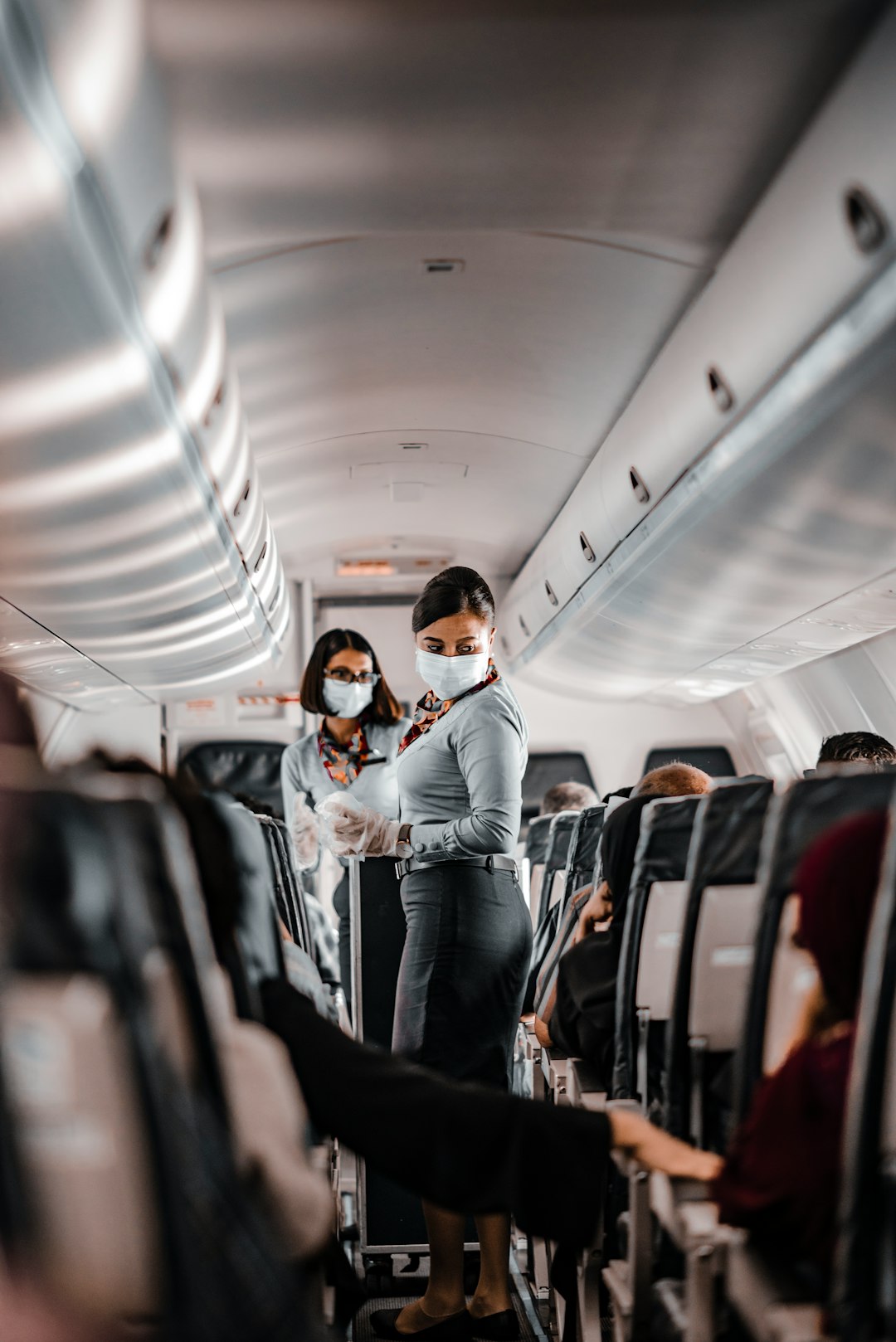 air hostess wearing a facemask standing in the aisle of an aeroplane