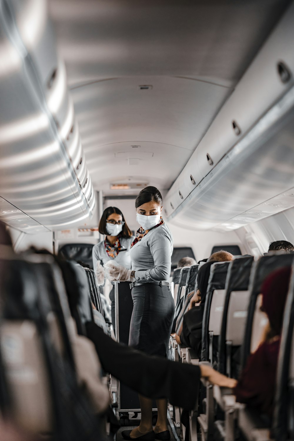 air hostess wearing a facemask standing in the aisle of an aeroplane