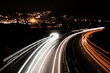 Wide shot of a tow truck driving along a highway with city lights in the background.