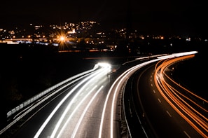 Wide shot of a tow truck driving along a highway with city lights in the background.