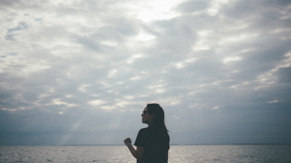 silhouette di donna in piedi sulla spiaggia durante il giorno