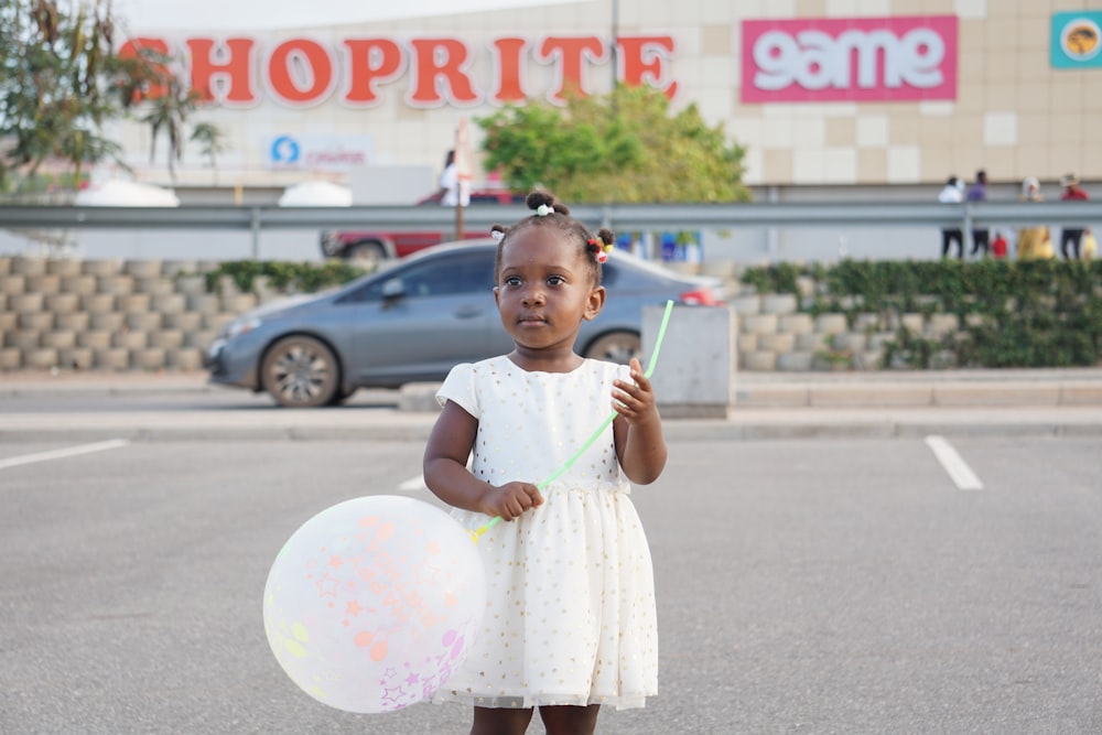 girl in white dress holding white and pink balloons