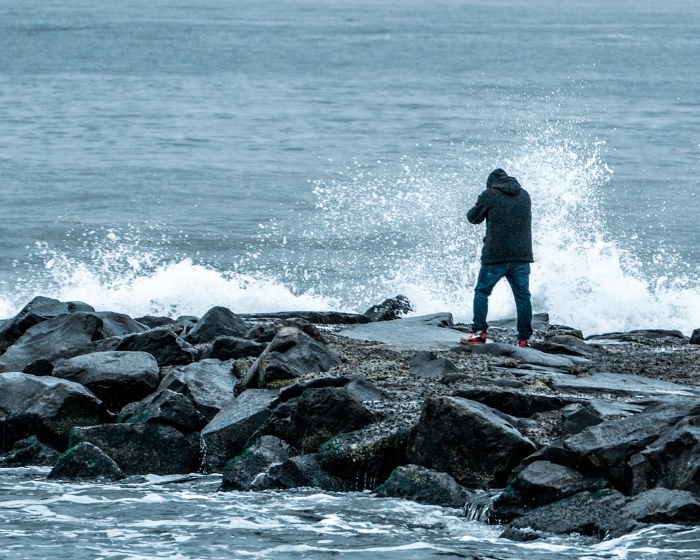 man in black jacket standing on rock near sea during daytime