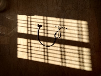 A stethoscope hangs on a wall, illuminated by sunlight streaming through blinds, casting striped shadows across the surface.
