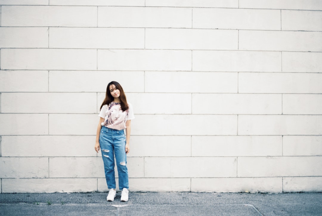 woman in white shirt and blue denim jeans standing beside white wall