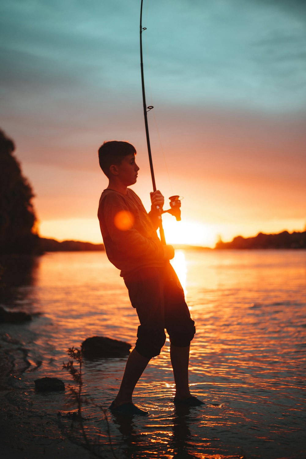 silhouette of man holding fishing rod during sunset