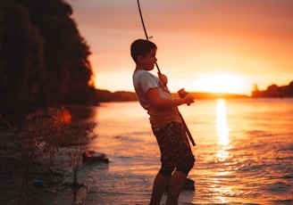 boy in white shirt and brown shorts holding fishing rod during sunset