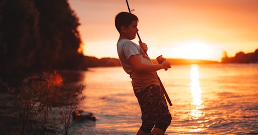 boy in white shirt and brown shorts holding fishing rod during sunset