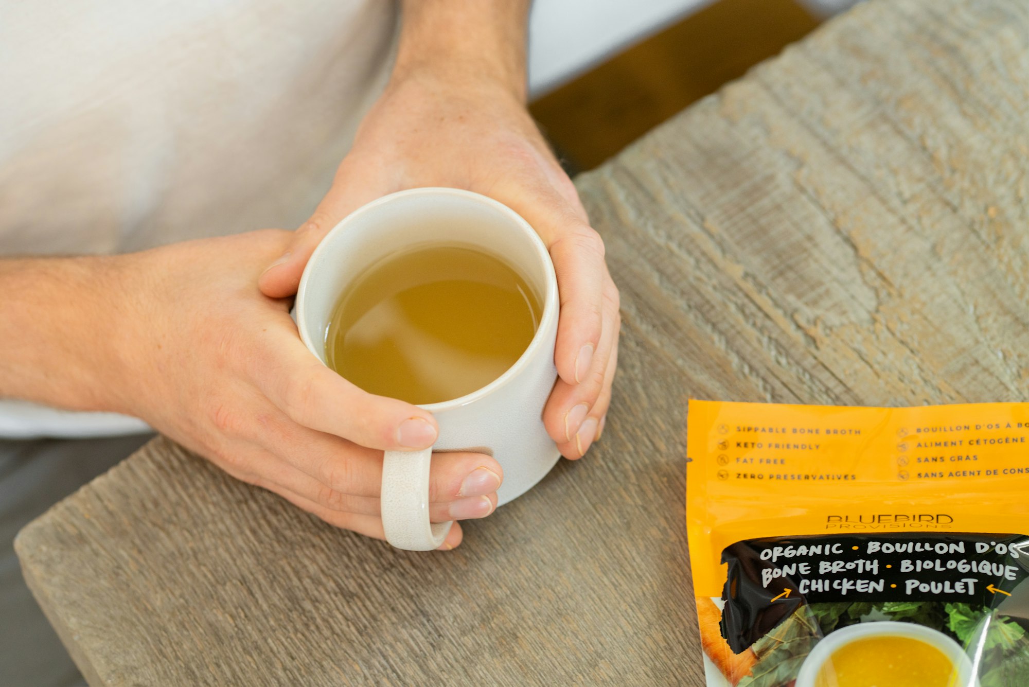 bone broth in white mug with hands wrapped around it 