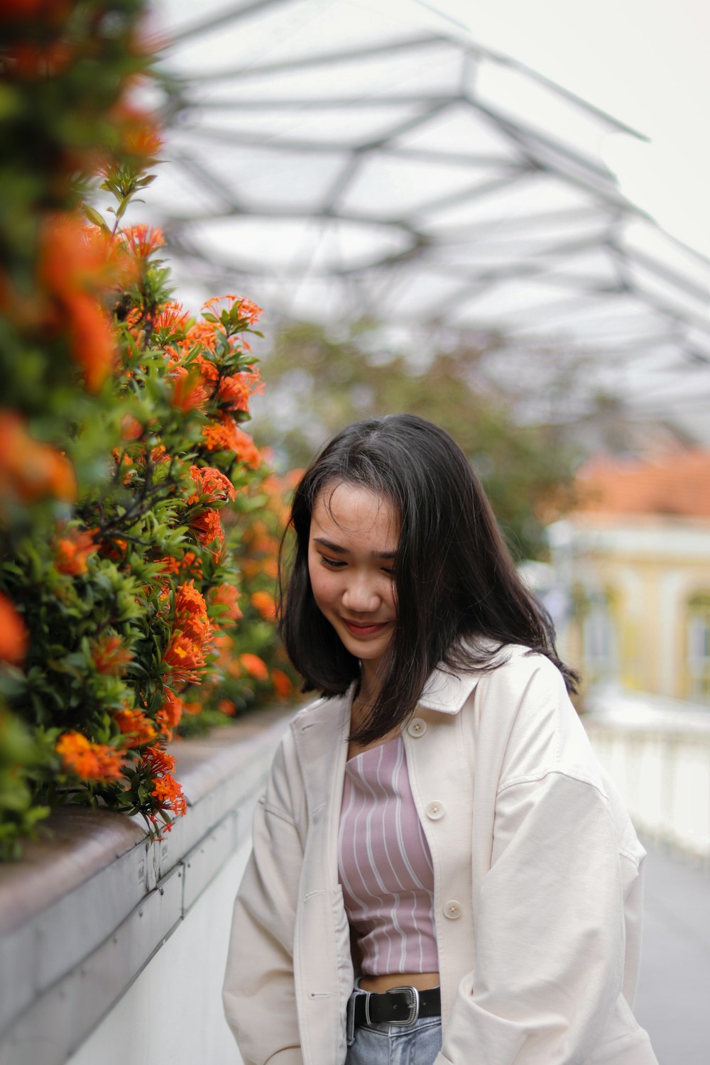 オレンジ色の花のそばに立つ白い長袖シャツの女性