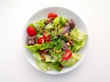 A premium salad featuring crisp greens, cherry tomatoes, nuts, and a light dressing in a stylish bowl.