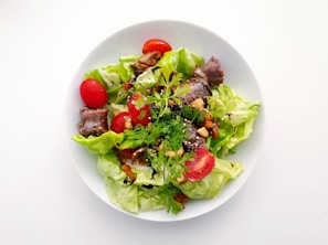A premium salad featuring crisp greens, cherry tomatoes, nuts, and a light dressing in a stylish bowl.
