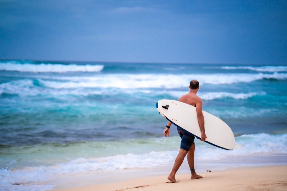 man in black shorts carrying white surfboard walking on beach during daytime