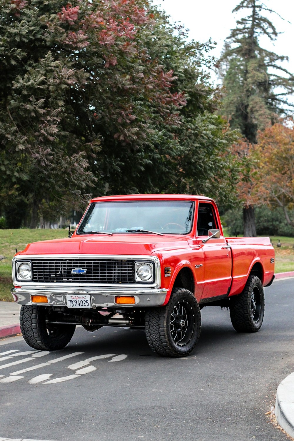 red chevrolet single cab pickup truck parked near green trees during daytime