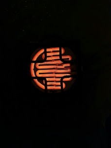 A glowing, spiral-shaped heating element is visible through a dark grid. The element emits a bright orange light, illuminating the surrounding area against a dark background.