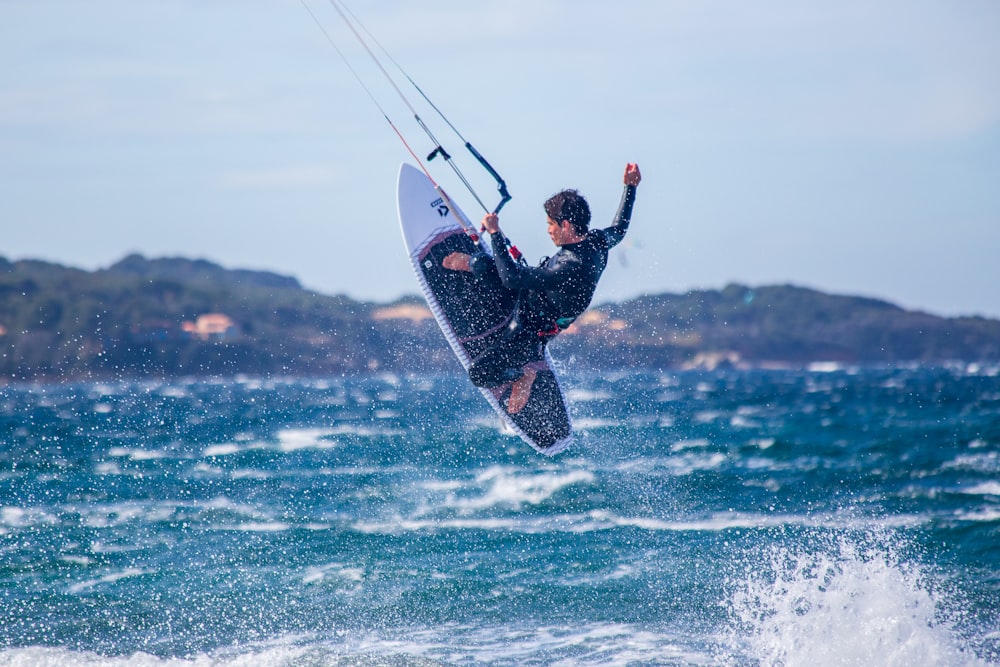 uomo in muta nera che fa surf sulle onde del mare durante il giorno