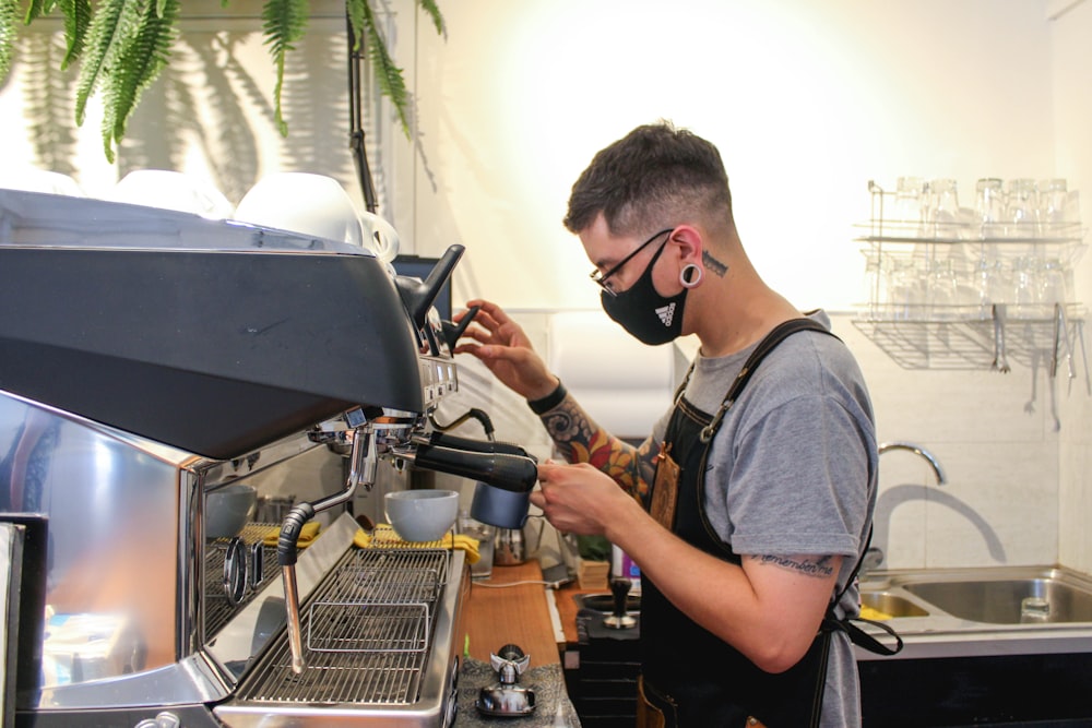 homme en t-shirt à col rond gris à l’aide d’une machine à expresso noire et grise