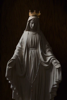 A white statue of the Virgin Mary wearing a gold crown and rosary beads