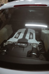 The image captures the engine bay of a car, showcasing a V8 FSI engine. The engine cover is prominently visible through the rear window, with a sleek design and branding that emphasizes its power and sophistication.
