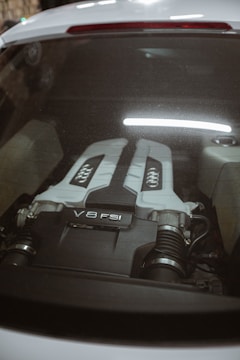 The image captures the engine bay of a car, showcasing a V8 FSI engine. The engine cover is prominently visible through the rear window, with a sleek design and branding that emphasizes its power and sophistication.