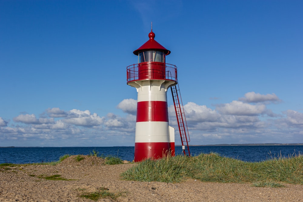 red and white lighthouse on green grass field under blue sky during daytime