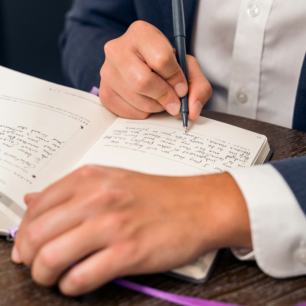 person in blue suit holding pen writing on white paper