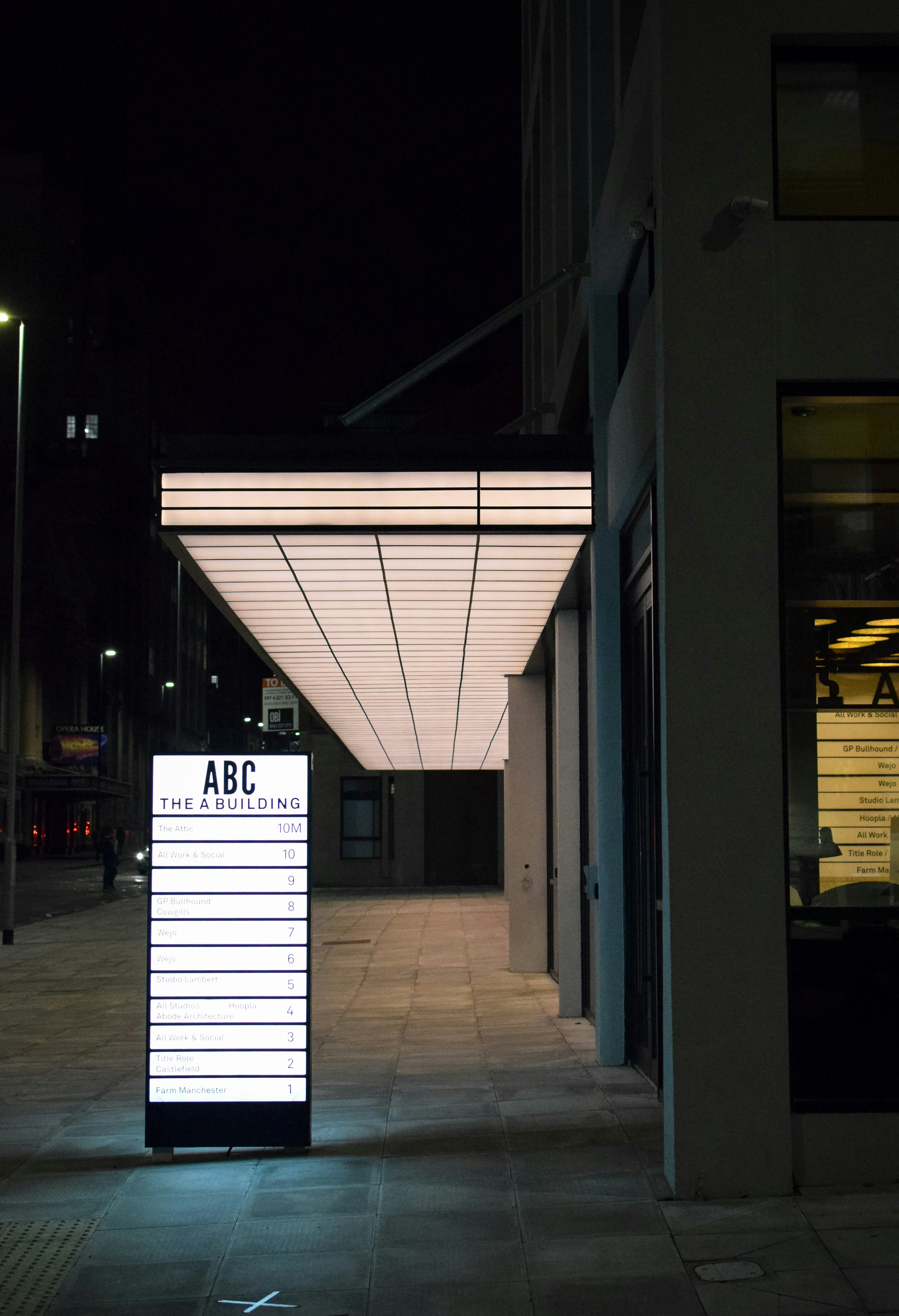 An illuminated directory sign stands before a modern office building.