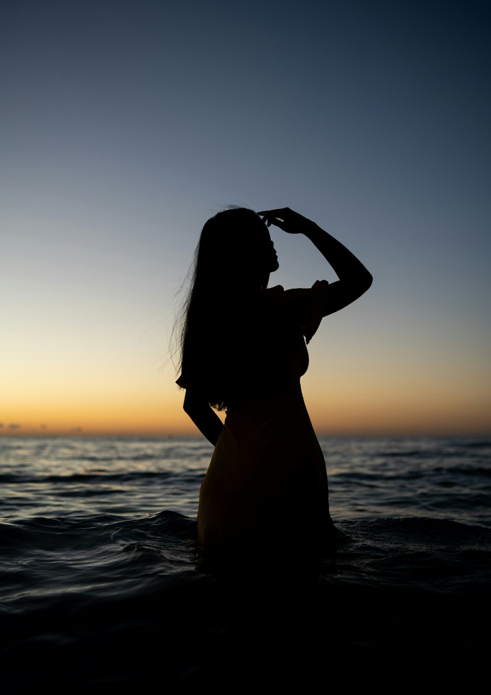 silhouette of woman standing on sea shore during sunset