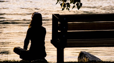 silhouette of person sitting on bench near body of water during daytime
